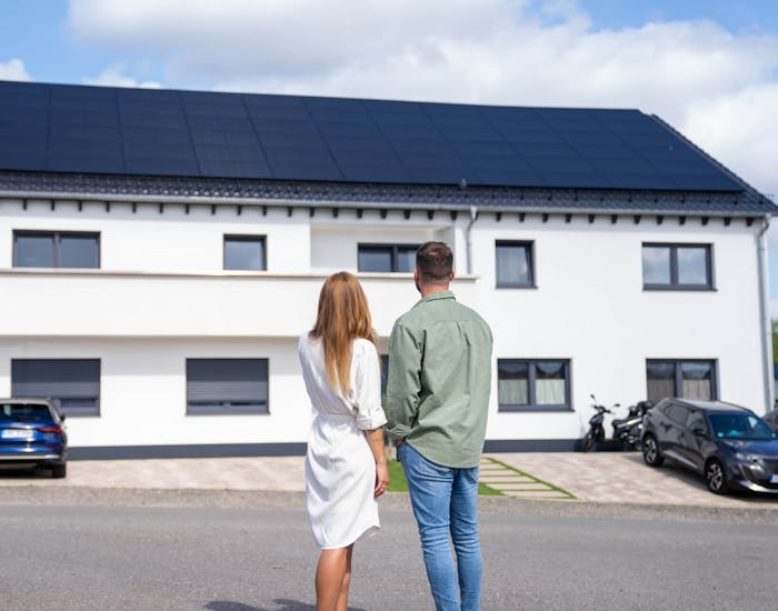 Paar schaut auf ein Mehrfamilienhaus mit Solaranlage auf dem Dach Paar schaut auf ein Mehrfamilienhaus mit Solaranlage auf dem Dach