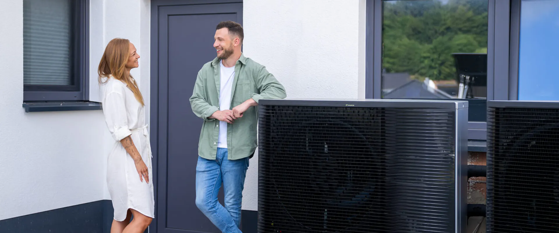 Paar steht vor Einfamilienhaus neben einer Wärmepumpe als steuerbare Verbrauchseinrichtung nach § 14a EnWG | Gelb Solar