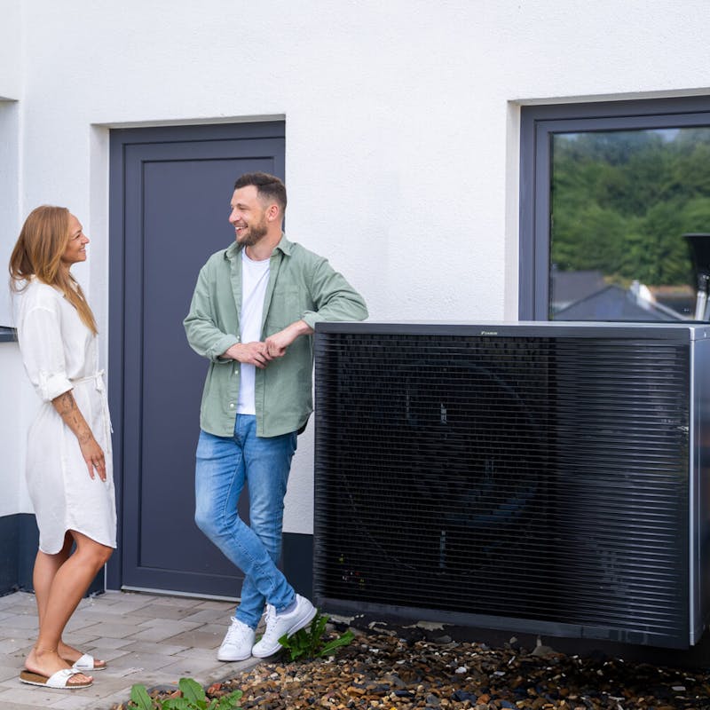 Junges Paar steht neben einer Wärmepumpe Junges Paar steht neben einer Wärmepumpe