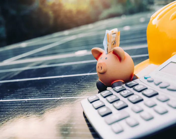 Sparschwein, Taschenrechner und Helm, die auf einer Solaranlage abgestellt sind Sparschwein, Taschenrechner und Helm, die auf einer Solaranlage abgestellt sind
