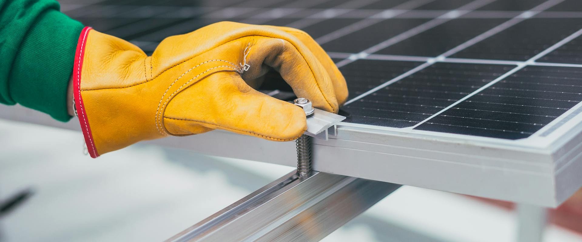 Hand eines Monteurs der per Aufdachmontage ein Solarmodul an eine Montageschiene verschraubt