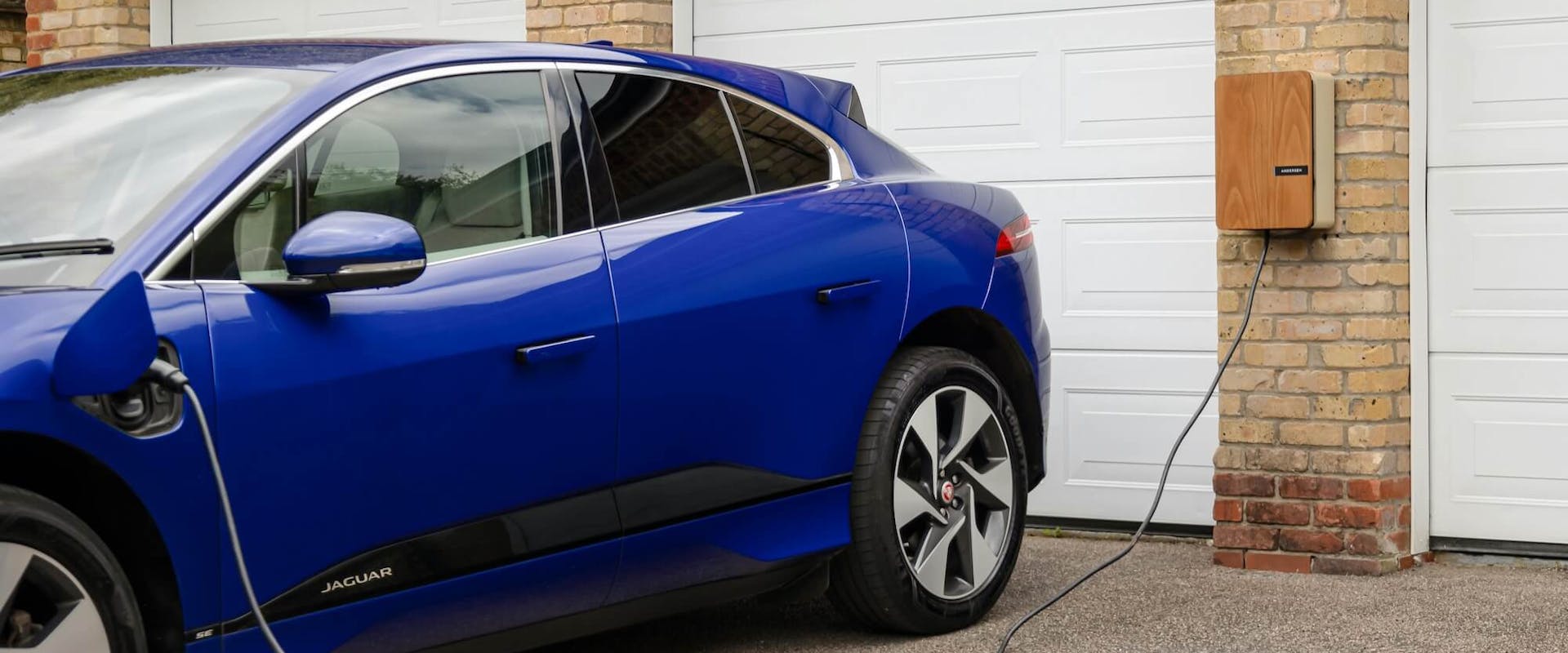Blaues Elektroauto lädt an einer Wallbox vor einer Garage Blaues Elektroauto lädt an einer Wallbox vor einer Garage