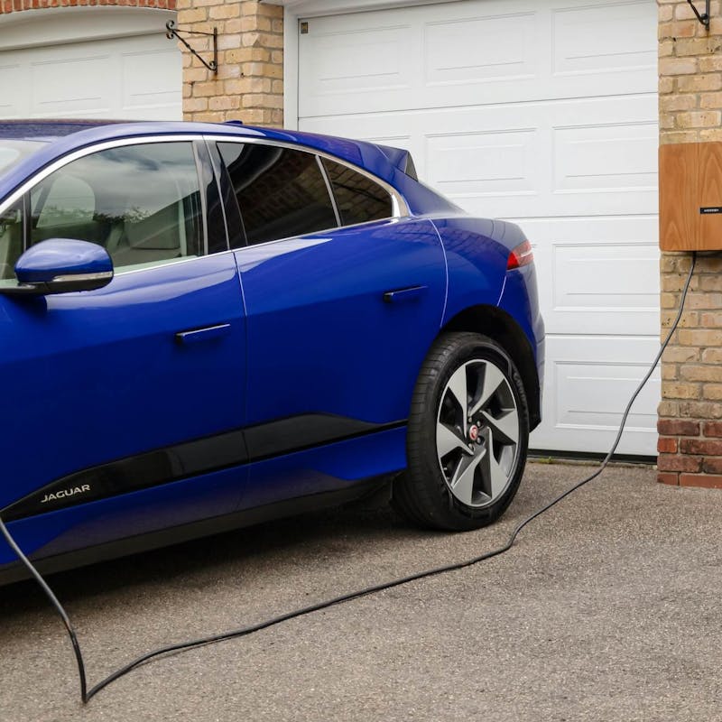 Blaues Elektroauto lädt an einer Wallbox vor einer Garage Blaues Elektroauto lädt an einer Wallbox vor einer Garage