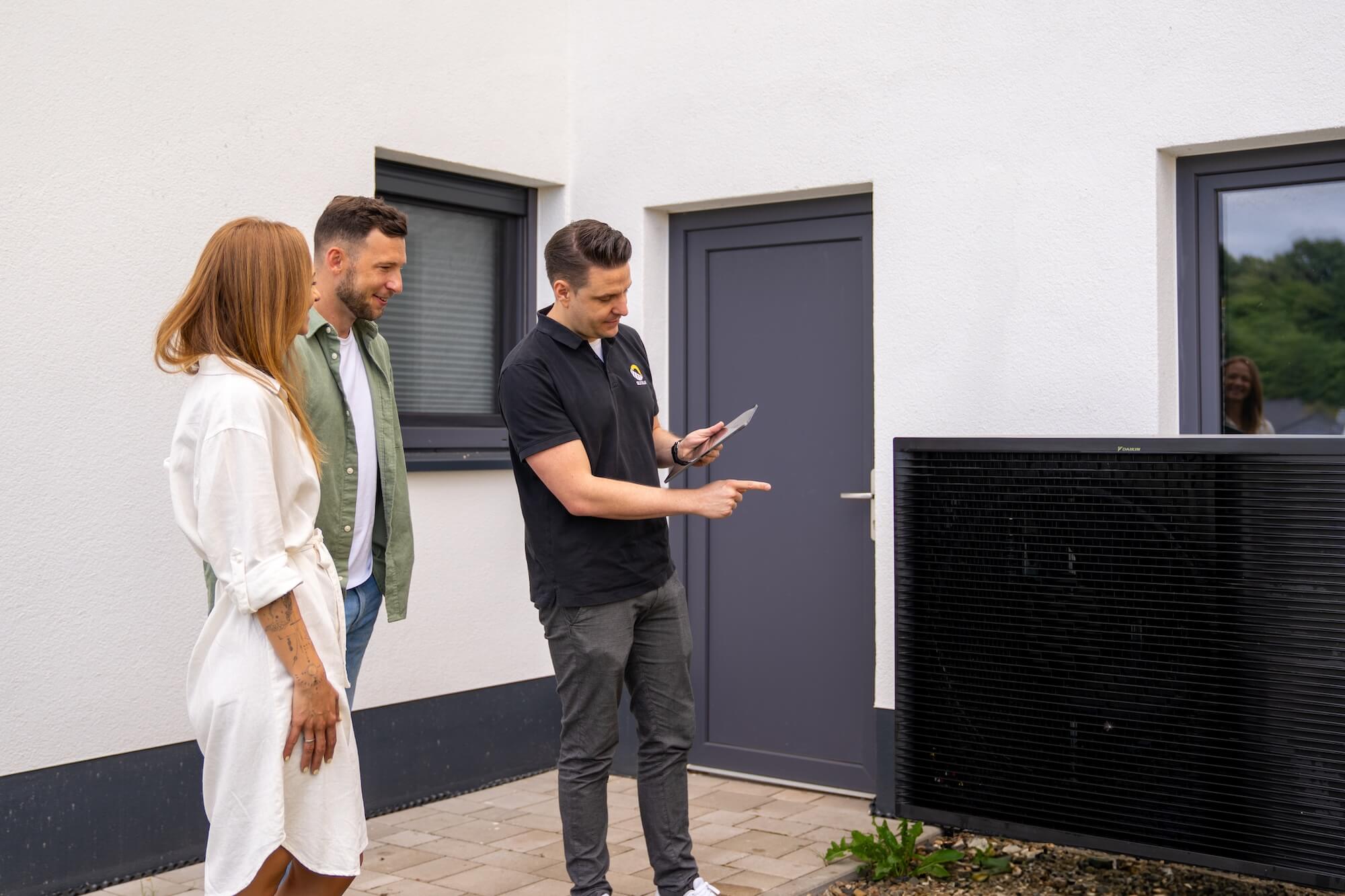 Paar wird von Solarexperten neben einer Wärmepumpe beraten