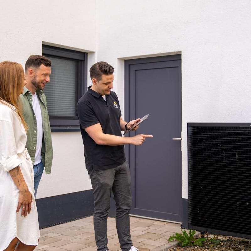 Paar wird von Solarexperten neben einer Wärmepumpe beraten Paar wird von Solarexperten neben einer Wärmepumpe beraten
