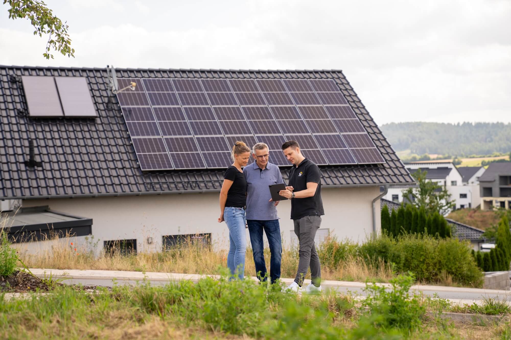 Paar wird vor Haus mit Solaranlage auf dem Dach von einem Gelb Solar Experten zu Stromspeicher beraten