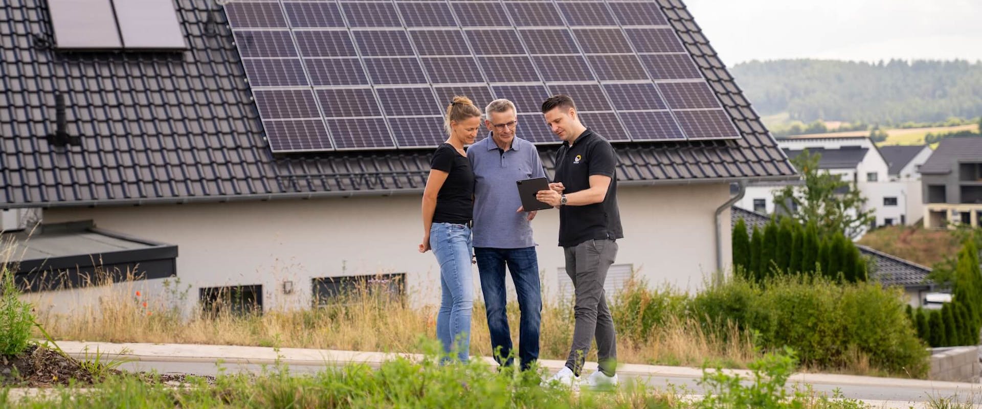 Paar wird vor Haus mit Solaranlage auf dem Dach von einem Gelb Solar Experten zu Stromspeicher beraten Paar wird vor Haus mit Solaranlage auf dem Dach von einem Gelb Solar Experten zu Stromspeicher beraten