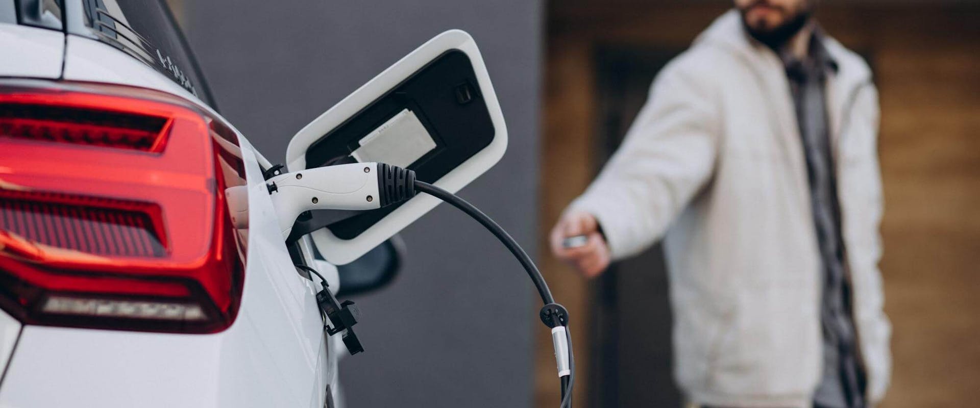 Mann steht neben seinem Elektroauto während es an einer Wallbox lädt Mann steht neben seinem Elektroauto während es an einer Wallbox lädt