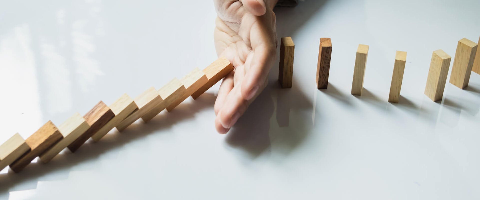 Person, die mit ihrer Hand eine Kette aus Dominosteinen stoppt