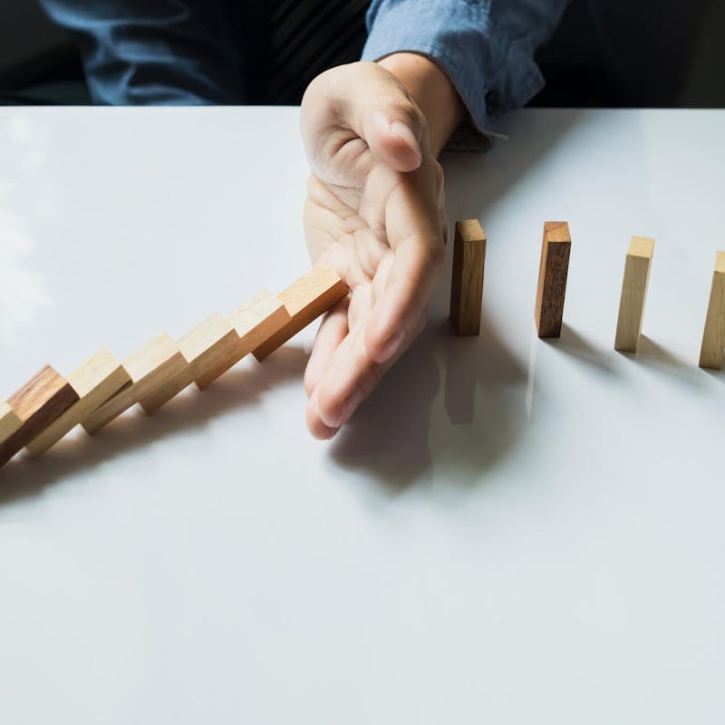 Person, die mit ihrer Hand eine Kette aus Dominosteinen stoppt