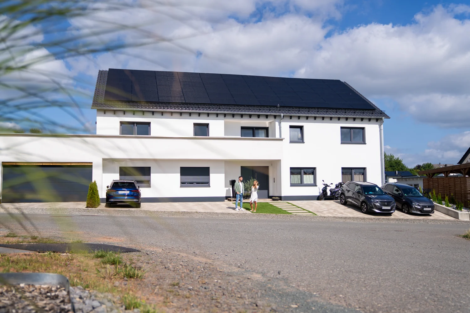 Einfamilienhaus mit All-Black-Solarmodulen auf dem Dach – Paar vor dem Haus blickt auf die Photovoltaikanlage | Gelb Solar