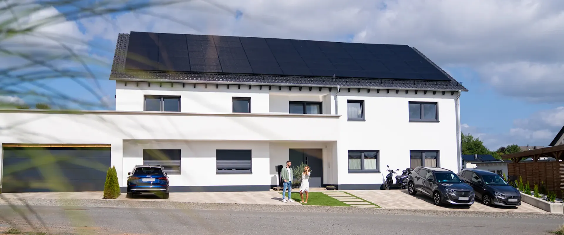 Einfamilienhaus mit All-Black-Solarmodulen auf dem Dach – Paar vor dem Haus blickt auf die Photovoltaikanlage | Gelb Solar Einfamilienhaus mit All-Black-Solarmodulen auf dem Dach – Paar vor dem Haus blickt auf die Photovoltaikanlage | Gelb Solar