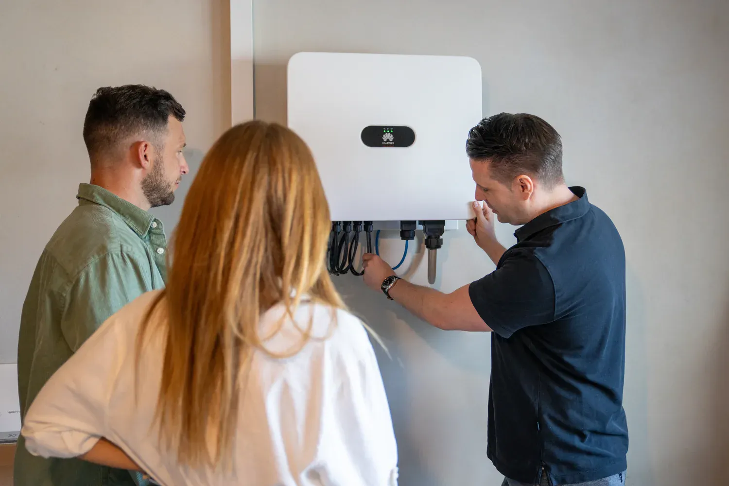 Fachmann erklärt Hausbesitzerpaar die Installation eines Huawei Wechselrichters an der Wand
