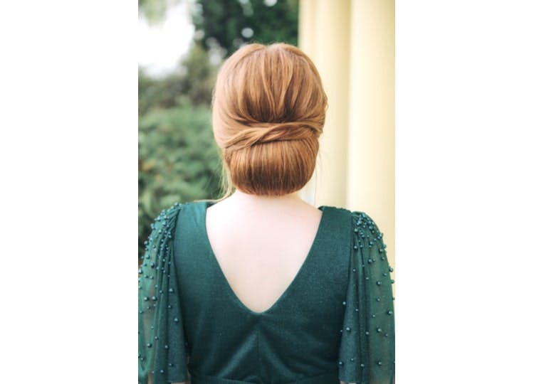 Arkası dönük duran kadının üzerinde yeşil, uzun kollu ve sırt dekolteli bir elbise bulunuyor. Kadının saçı, chignon saç stili olarak aşağıdan toplanmış bir şekilde duruyor.