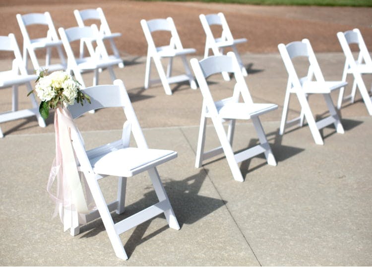 Açık bir alanda bulunan beyaz sandalyelerin her biri arasında belirli bir mesafe bulunuyor. Bir sandalyede beyaz bir gelin çiçeği duruyor.