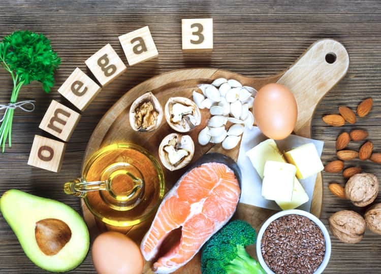 Ahşap bir masa üzerinde; maydanoz, avokado, balık, yumurta, sıvı yağ, ceviz, badem, brokoli, kaşar peyniri ve omega 3 yazısı bulunuyor.