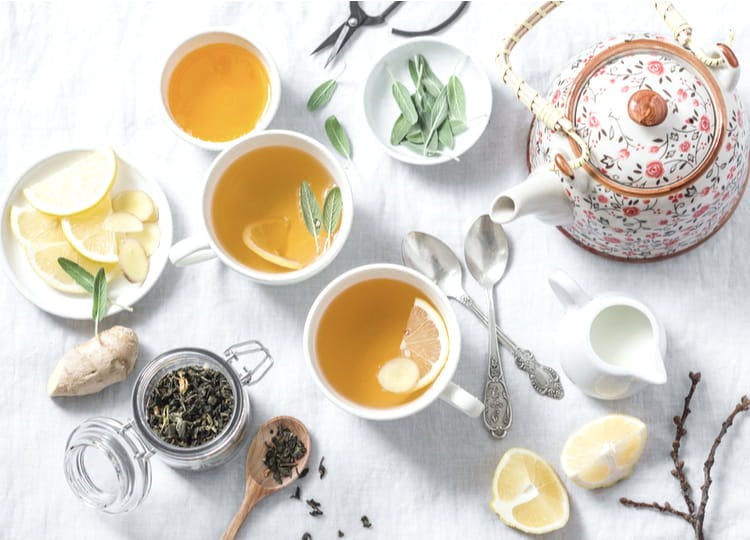 Açık renk arka plan üzerinde; çaydanlık, bir kavanoz içinde yeşil çay, limonlar, içinde dilimlenmiş limonların bulunduğu bir tabak, çay kaşıkları ve içinde yeşil çay olan fincanlar bulunuyor.
