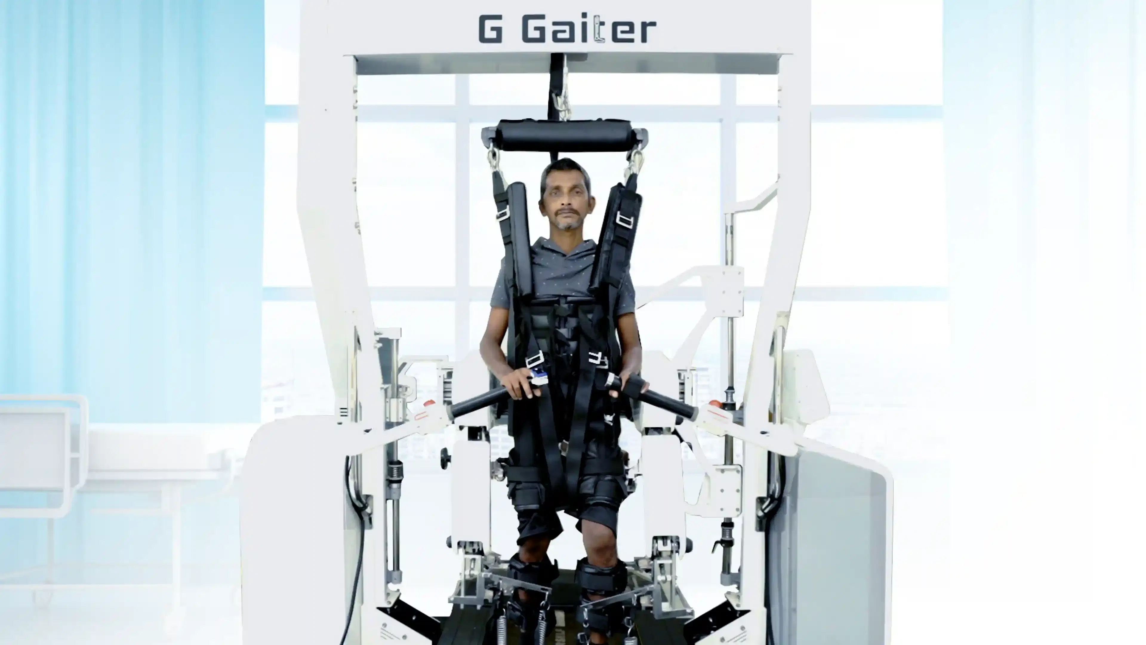 Patient undergoing robotic-assisted gait training on the G Gaiter system at General Hospital Thiruvananthapuram, supported by suspension harness and guided lower-limb movement.