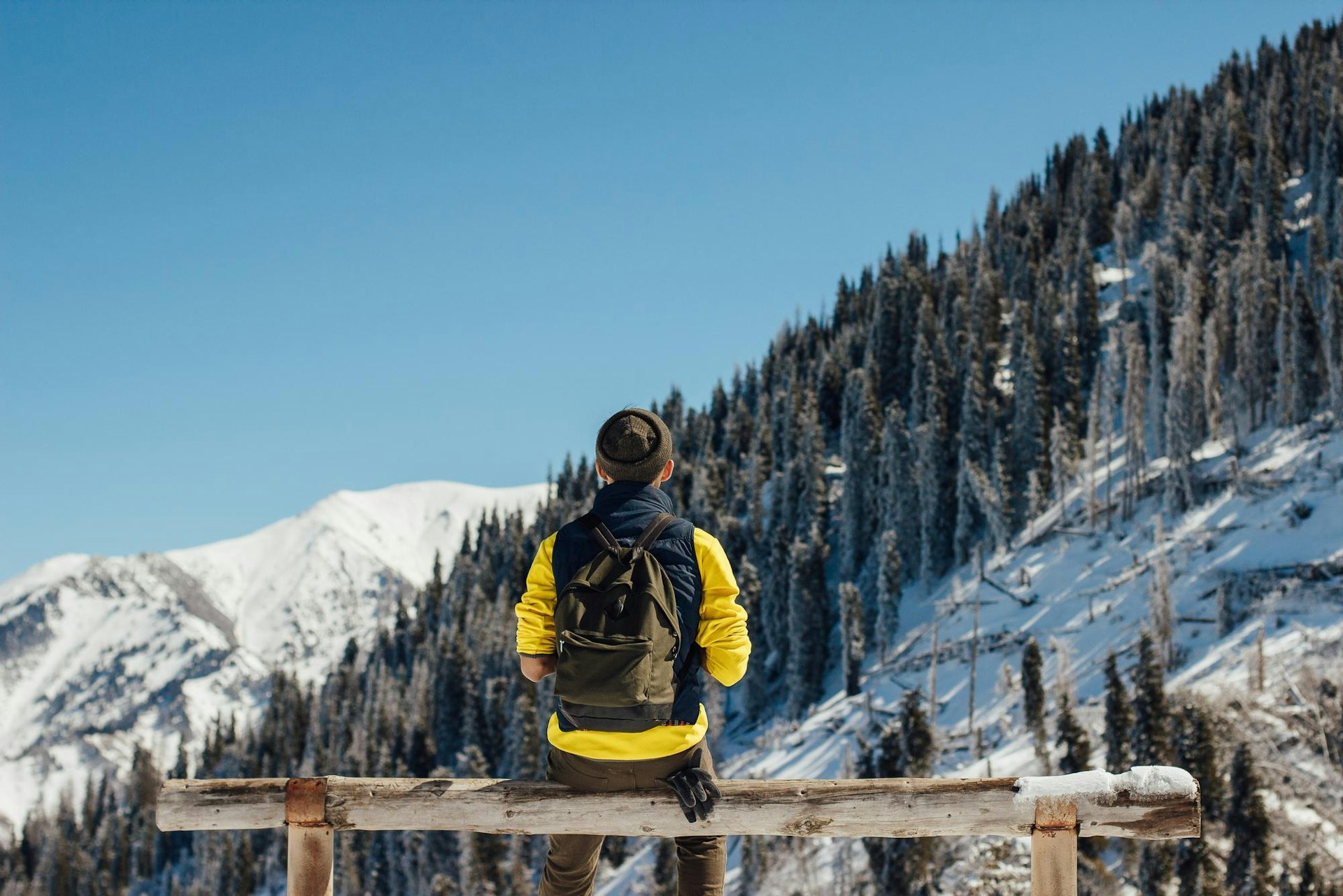 Male in yellow sweater and carrying a black backpack sitting on a bench, gazing at the slopes at Whistler Blackcomb in British Columbia, Canada.