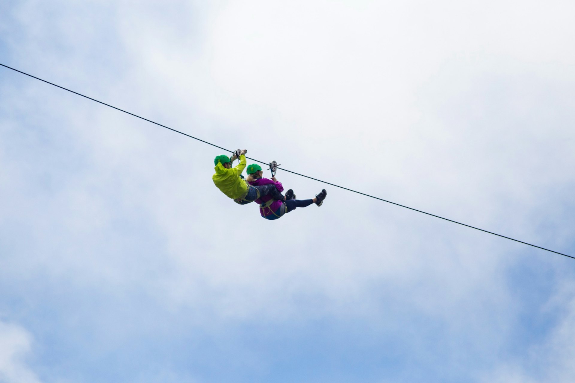 Adventurous tourist zip lining against cloudy sky