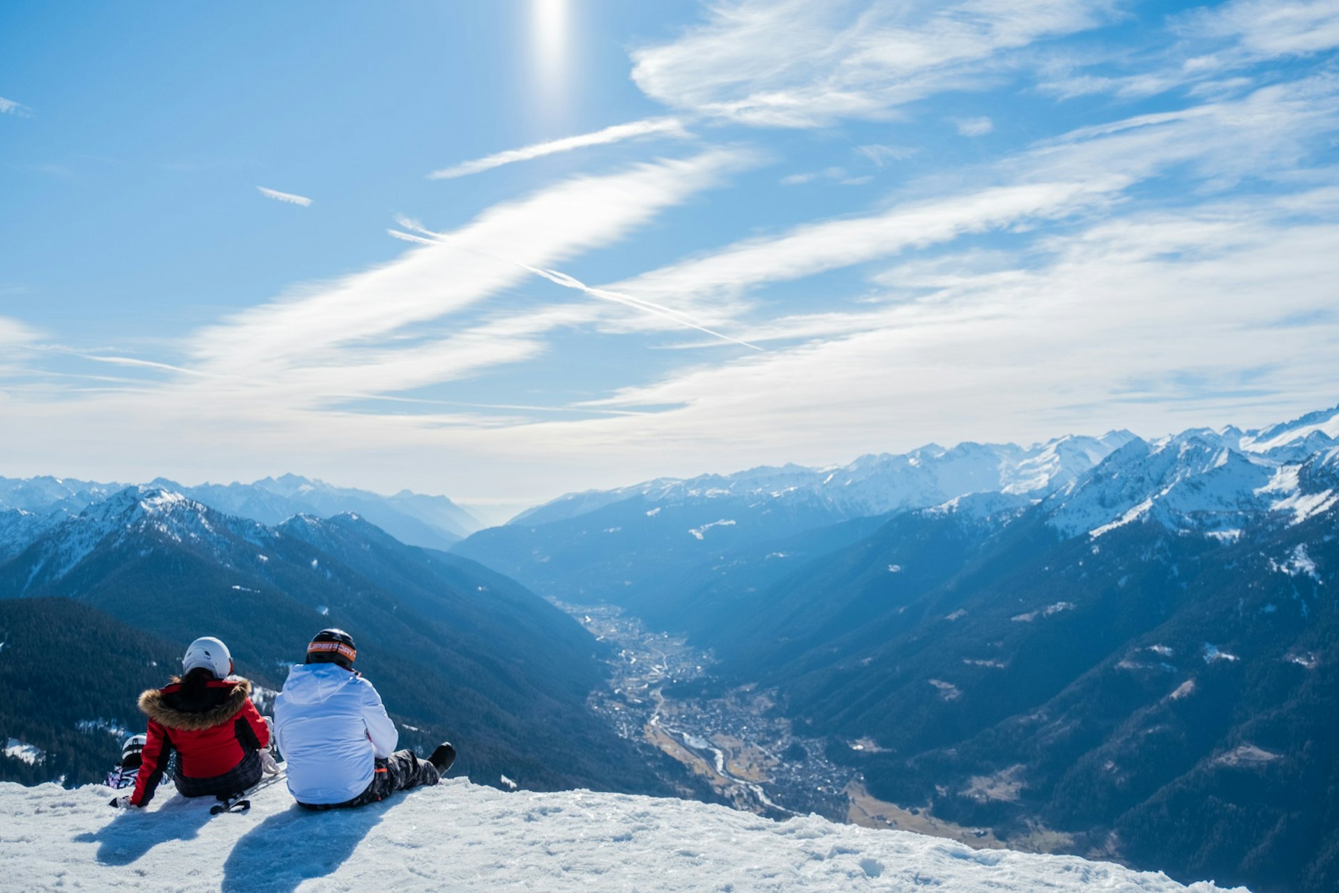 A ski couple in colorful ski attire sitting on the slopes, gazing at the horizon, at Whistler Blackcomb in British Columbia, Canada.