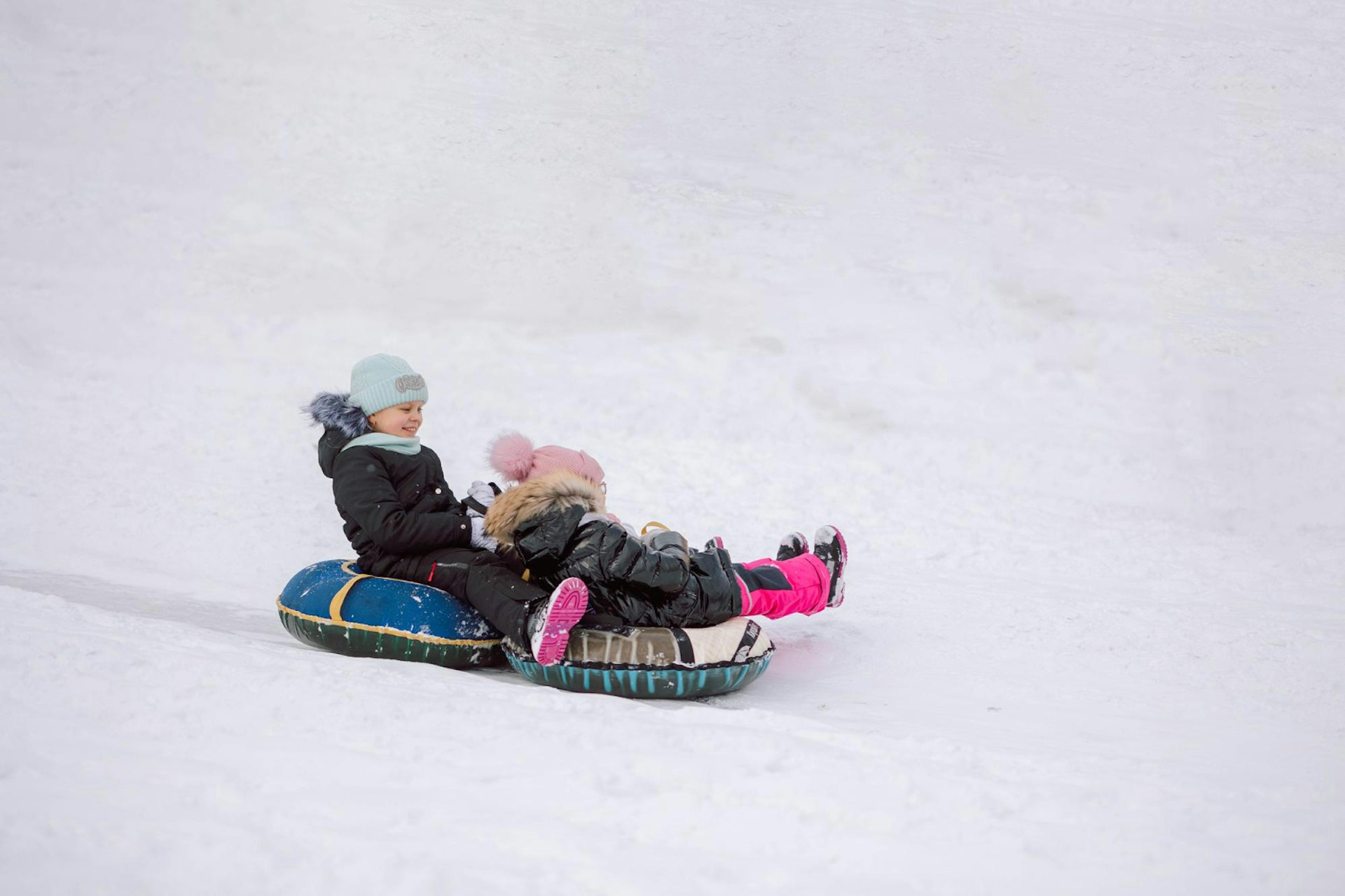 Little girls sledding down hill on walk in winter snowy day