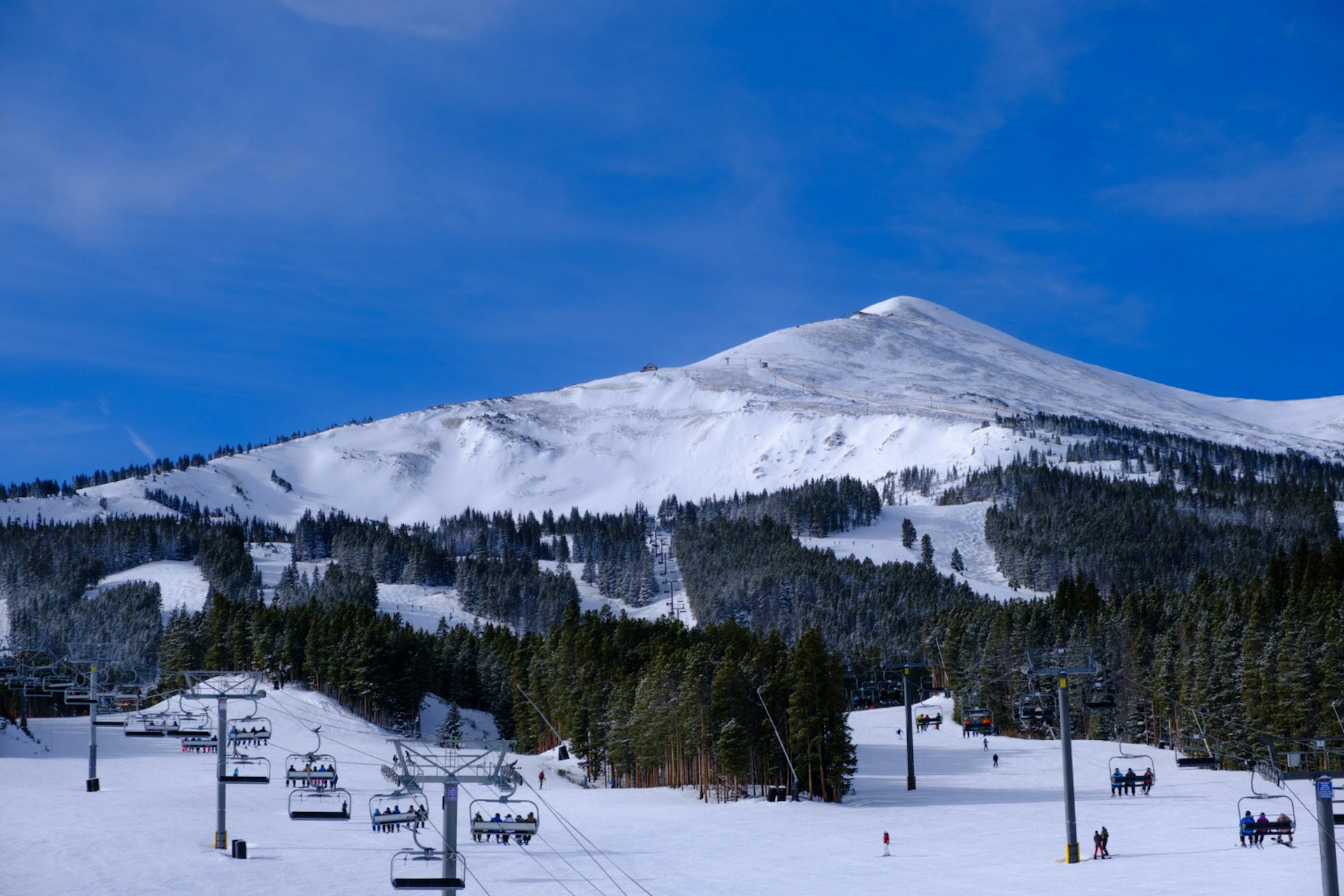 Landscape of ropeways surrounded by hills and forests covered in the snow under a blue sky