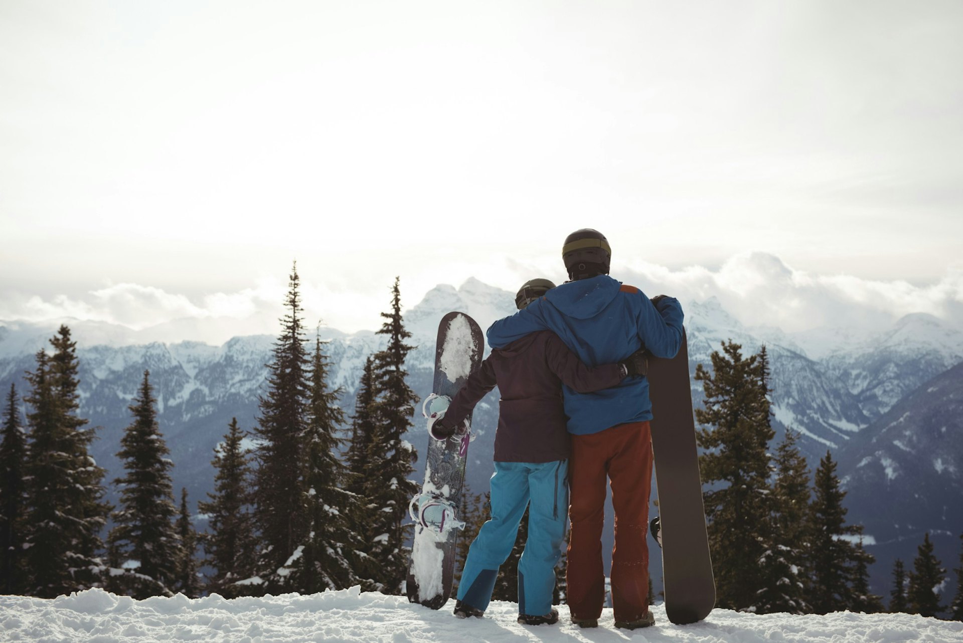 Rear view of couple holding snowboard at mountain during winter against sky