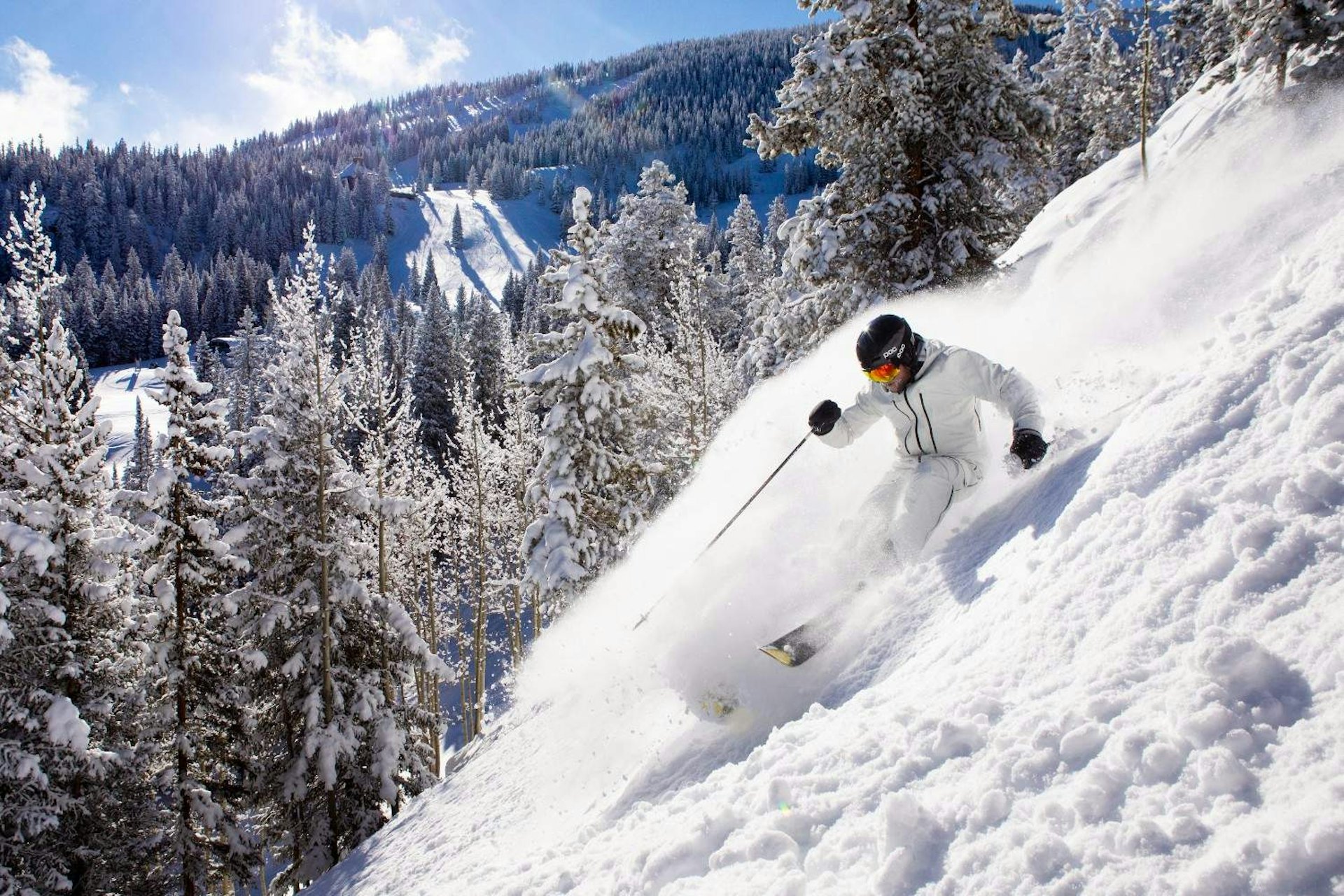 Male skier in white ski attire hitting the slopes at Snowmass in Colorado, USA.