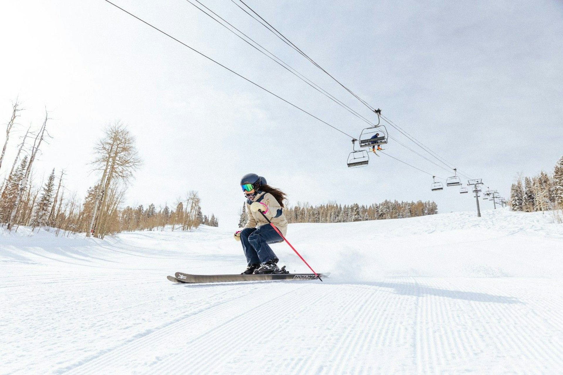 Female skier in white and blue ski attire hitting the slopes at Snowmass in Colorado, USA.