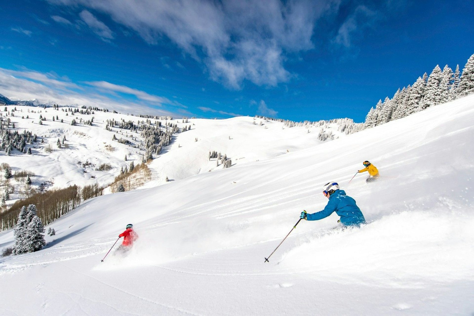 Three individuals ski down a snowy slope, surrounded by a picturesque winter landscape.