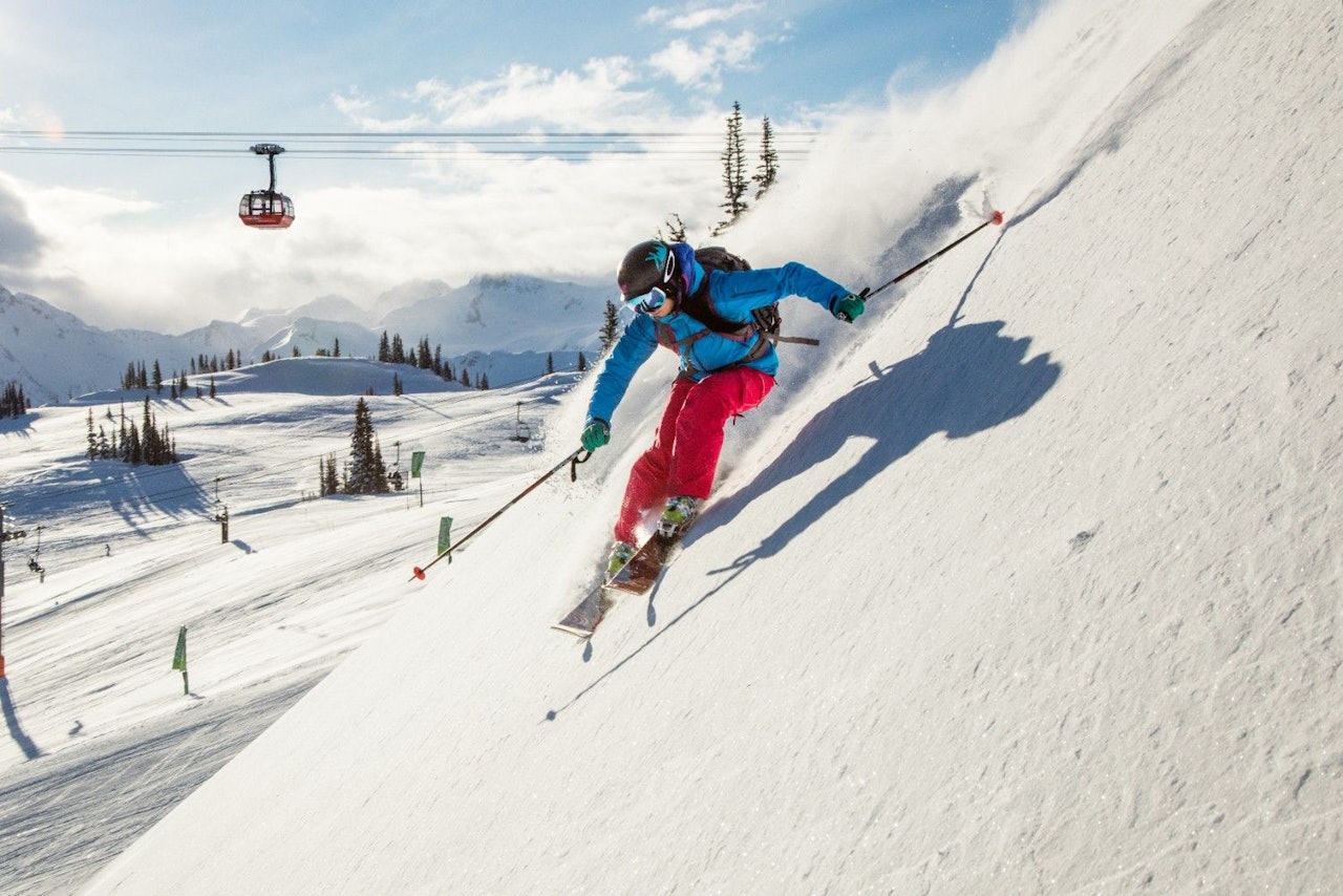 Skier of undiscernible gender in blue ski jacket and red ski pants hitting the slopes at Whistler Blackcomb in British Columbia, Canada.