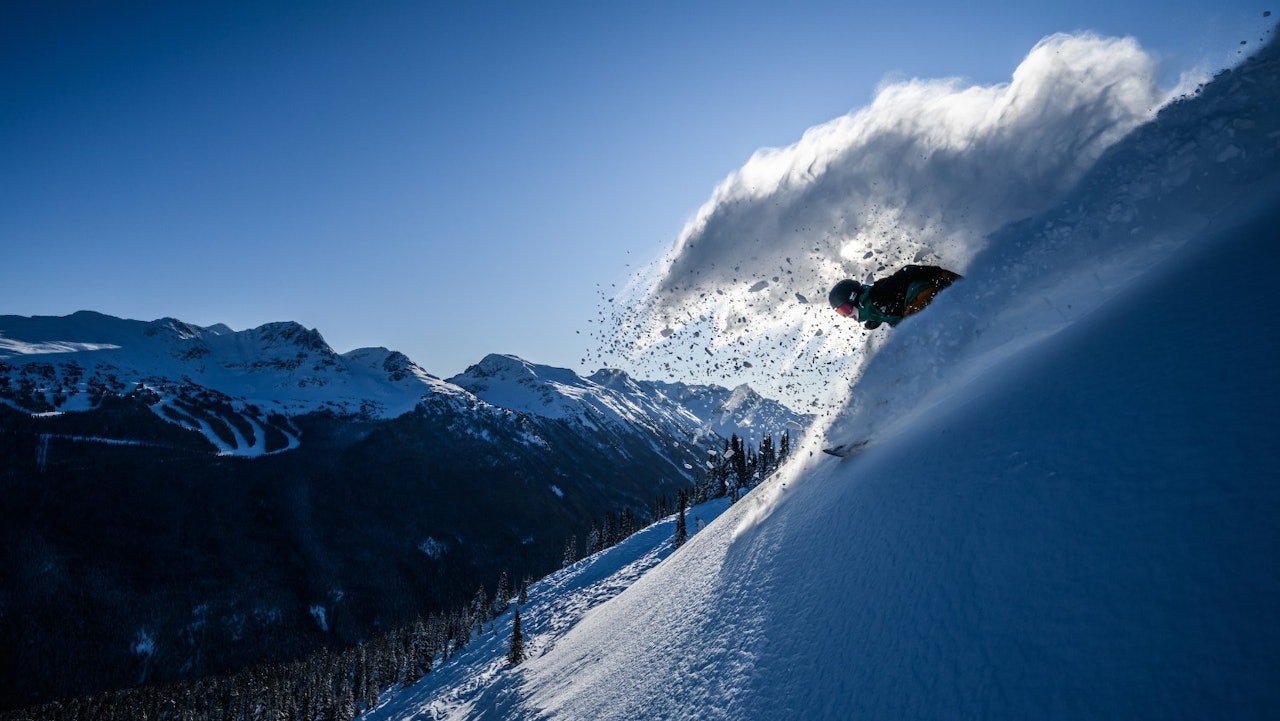 Snowboarder of undiscernible gender in dark colored ski attire hitting the slopes on Whistler Mountain at Whistler Blackcomb in British Columbia, Canada.