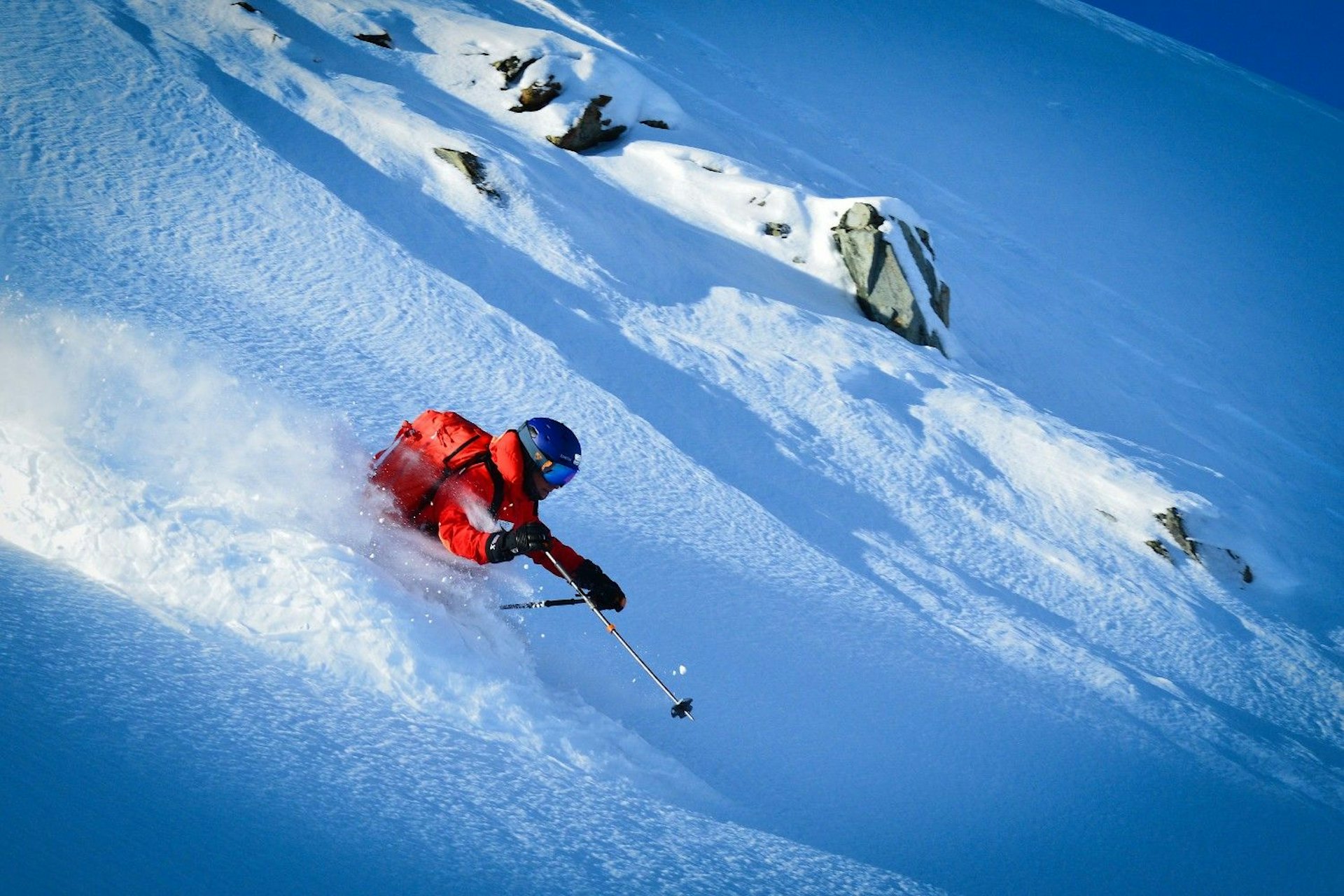 Skier of undiscernible gender in orange ski attire partaking in heli-skiing at Whistler Blackcomb in British Columbia, Canada.