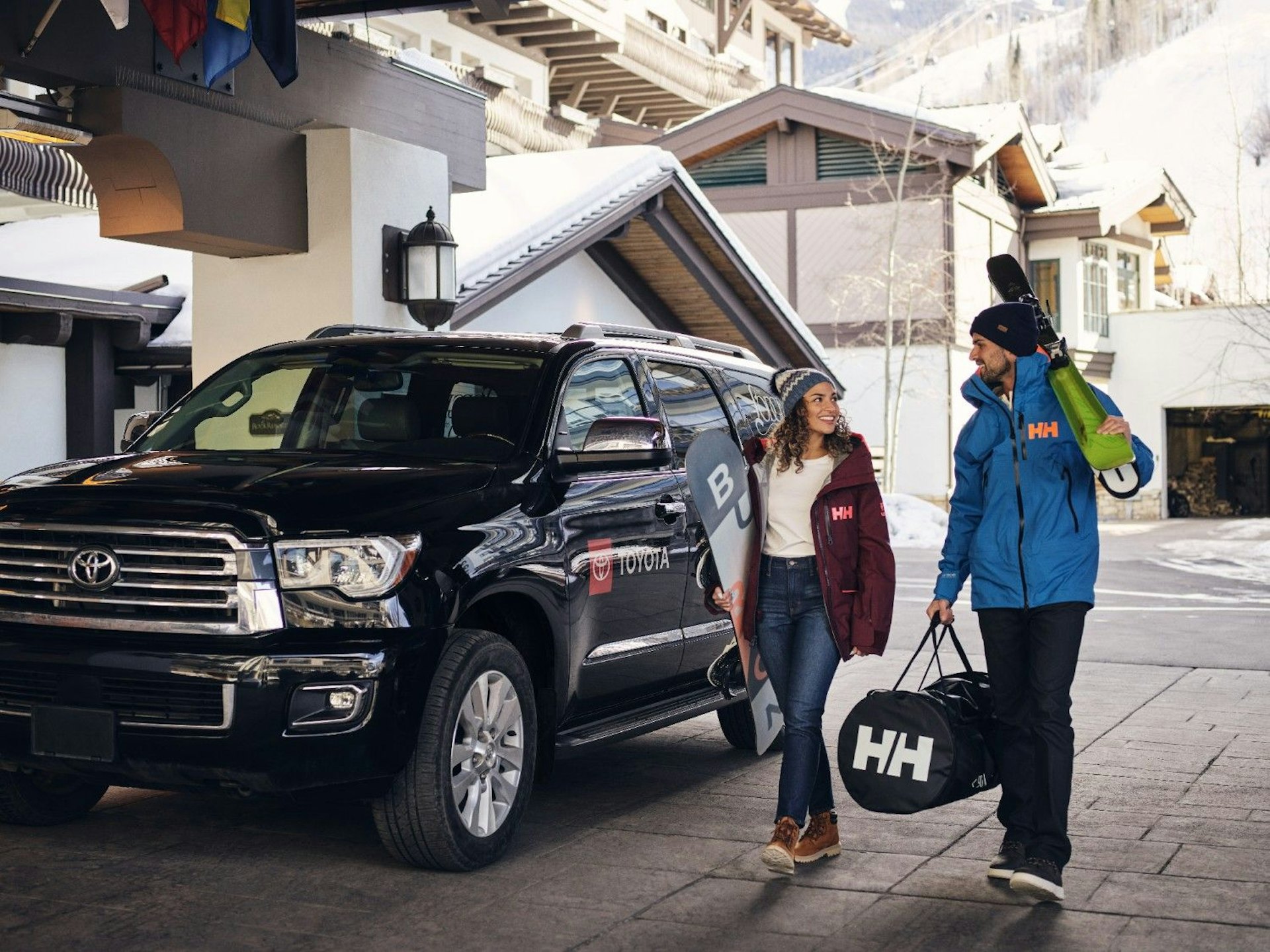 A man and woman stand beside a black SUV, smiling and engaged in conversation.