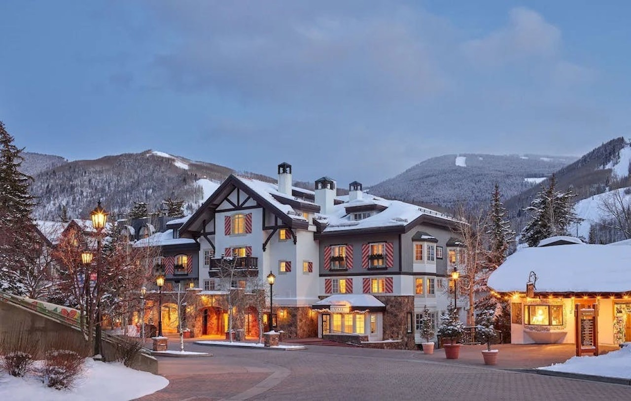The St. Regis Aspen, a luxury hotel surrounded by snow-capped mountains and lush trees, showcasing its elegant architecture.