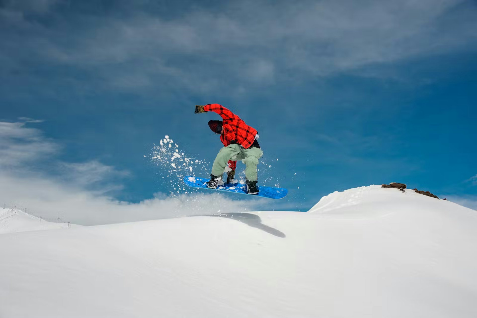 A snowboarder performs a jump in mid-air above a snowy slope, showcasing skill and excitement in winter sports.