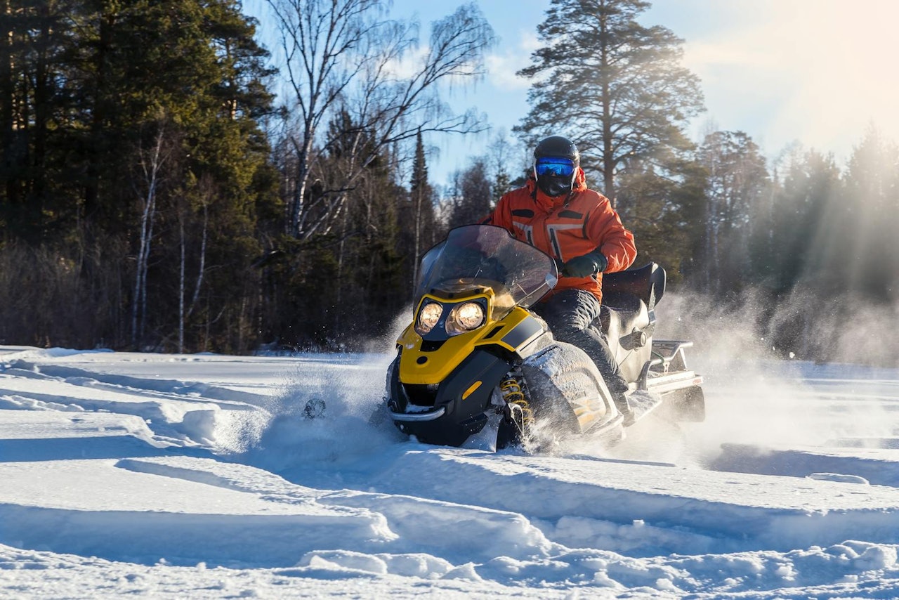 A man riding a snowmobile across a snowy landscape, leaving tracks in the fresh snow.