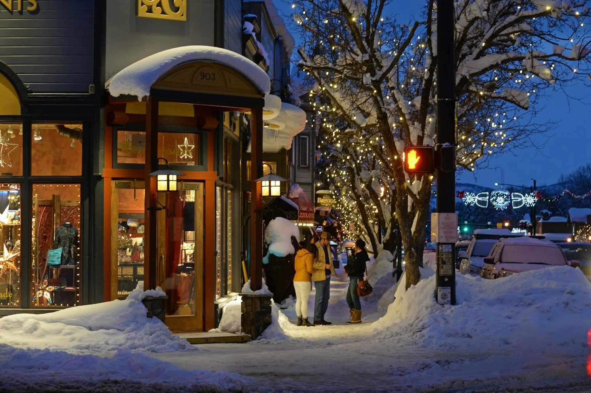 A snow-covered street at night featuring a warmly lit storefront, creating a cozy winter atmosphere.