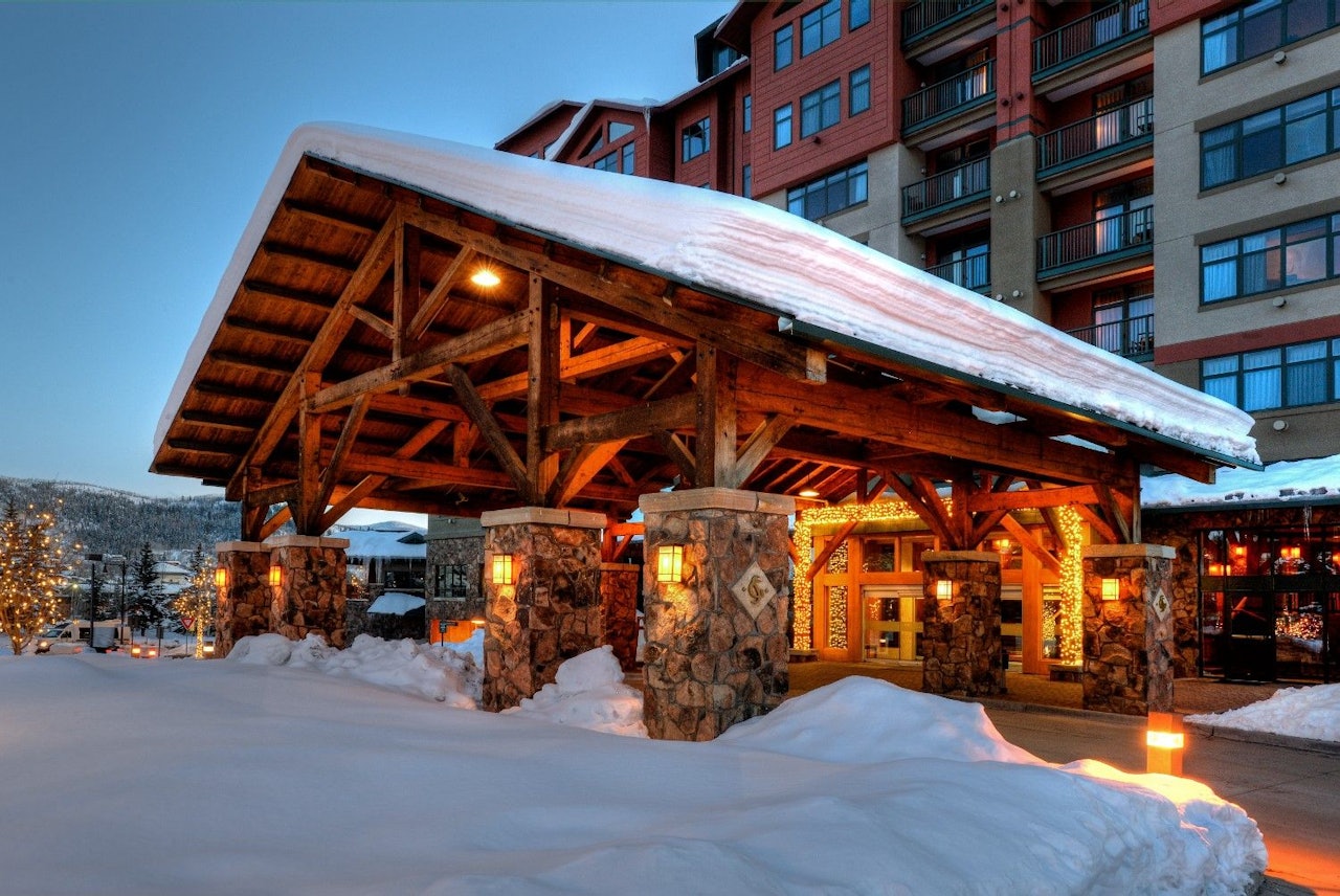 A cozy lodge surrounded by snow, illuminated by warm lights, creating a welcoming winter atmosphere.