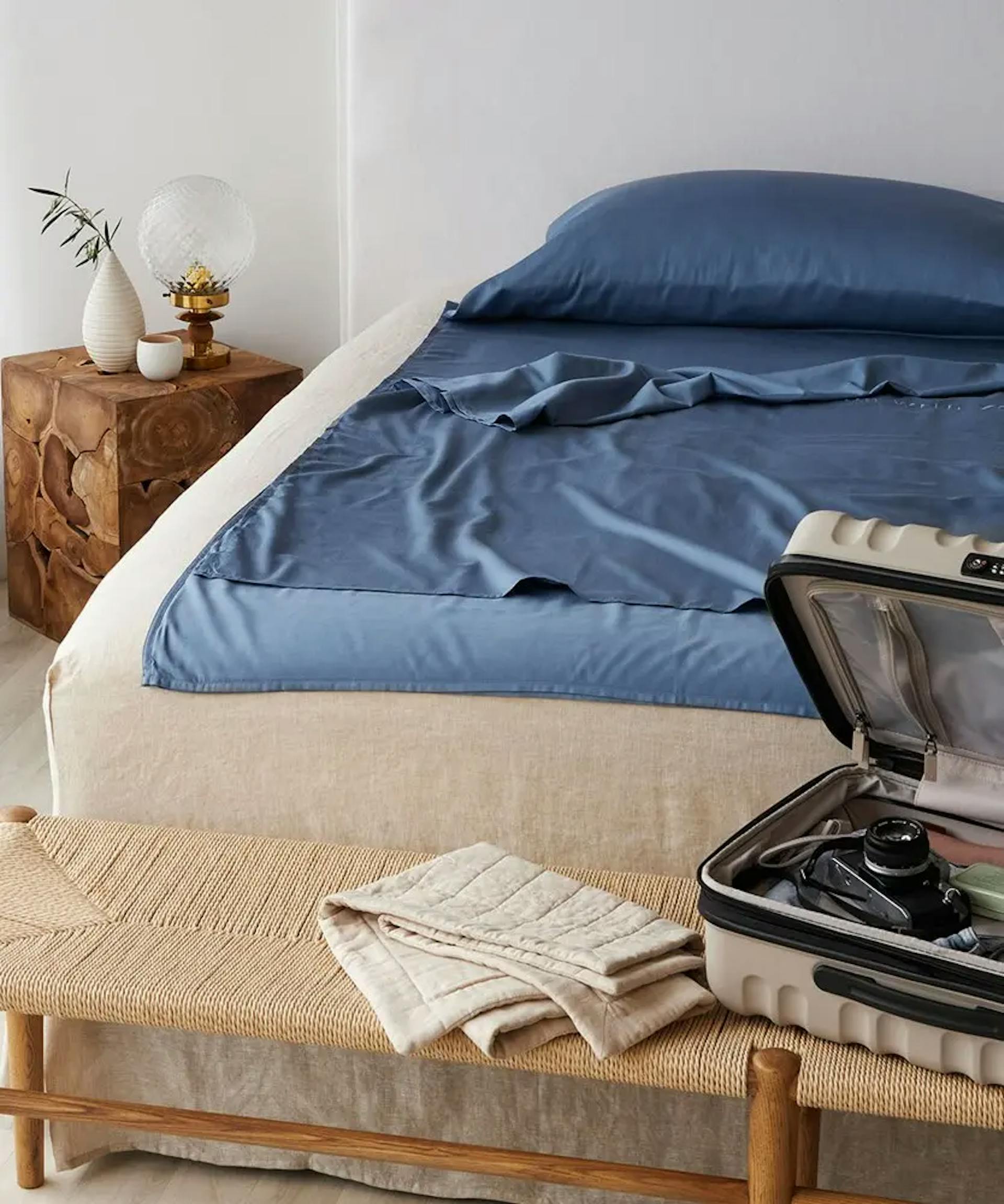 Blue Travel Sheets on bed with suitcase 