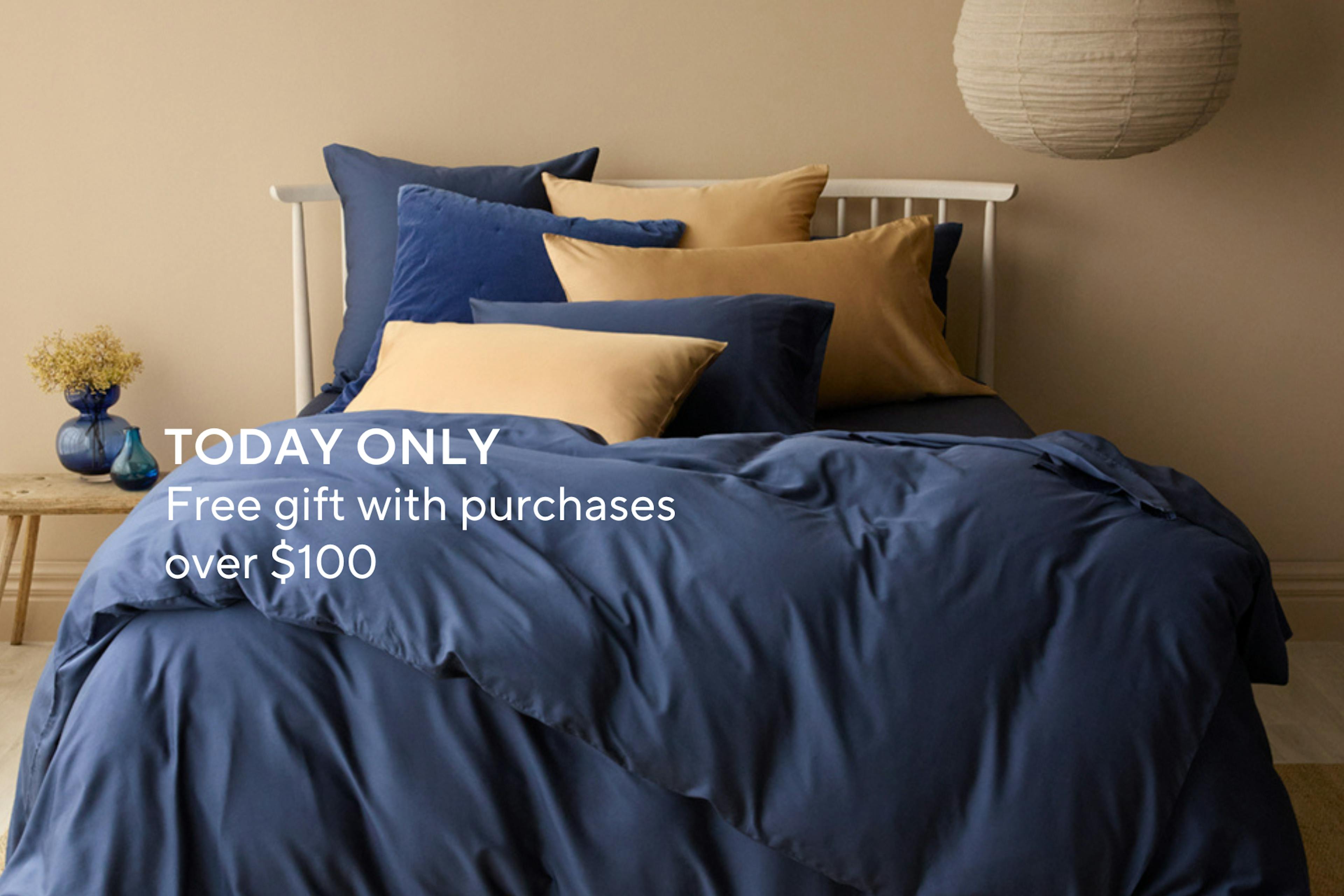 Navy and gold bedding set on a styled bed with text promoting a free gift offer for purchases over $100 for cyber monday
