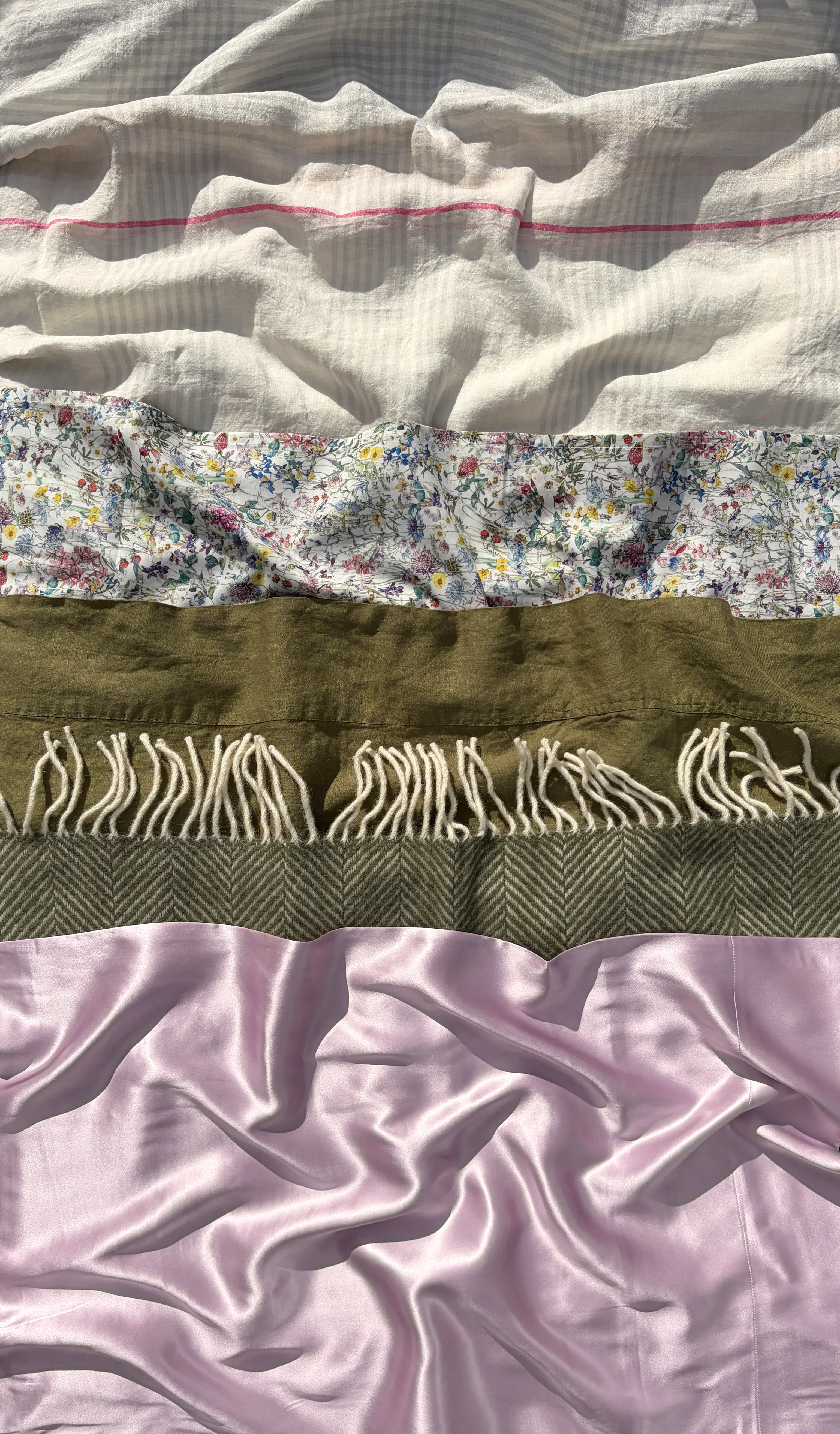 a flatlay of layered fabrics including striped white linen, floral print, green wool, and lilac satin