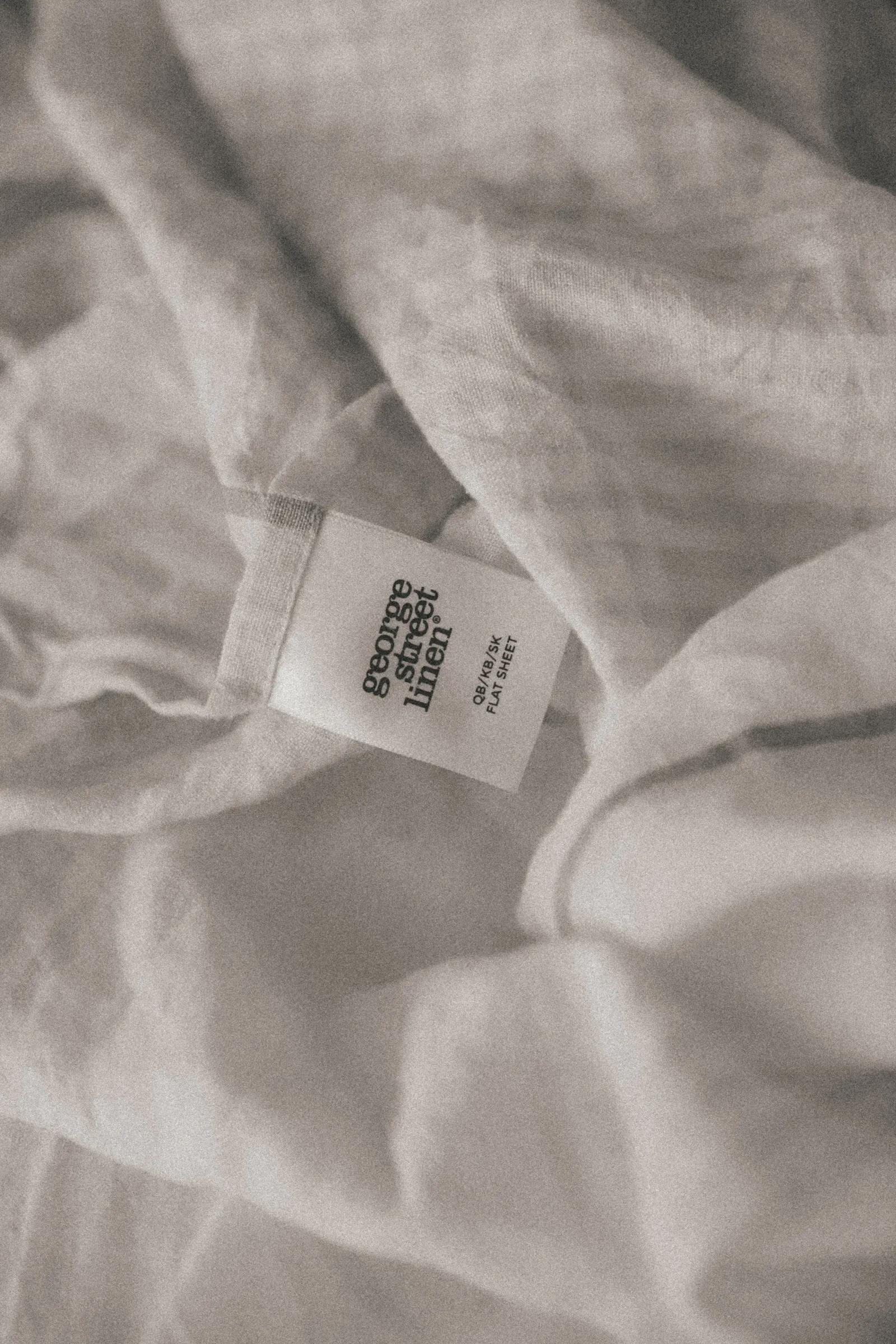 close-up of a crumpled white linen flat sheet displaying a product tag from "george street linen"