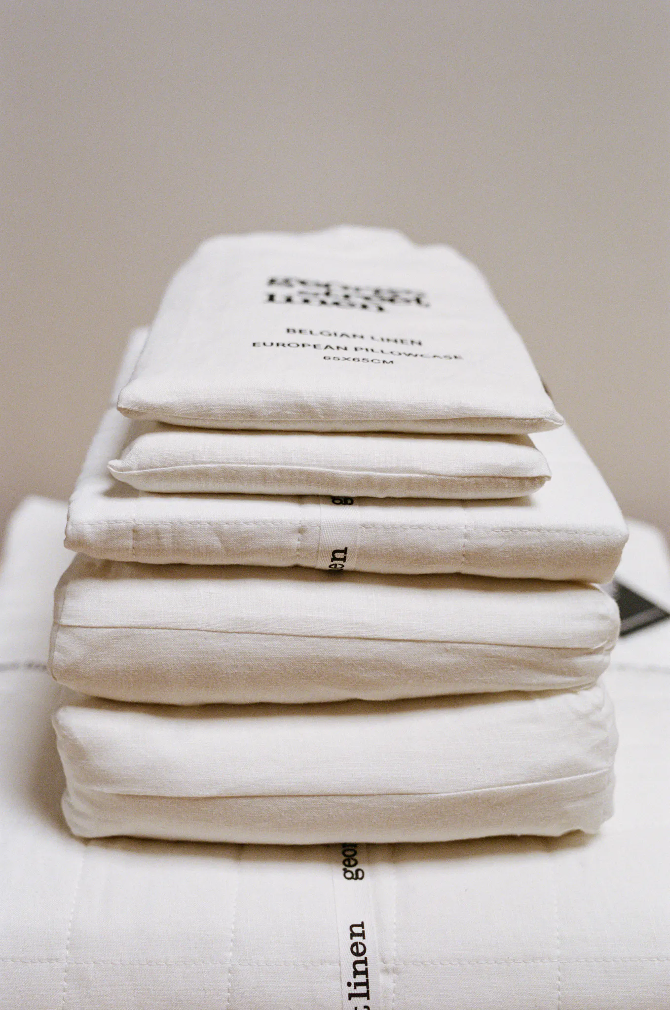 A stack of folded white George Street Linen Belgian linen bedding, with a labeled European pillowcase bag on top.
