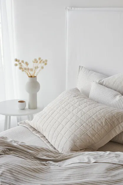 Cotton jersey bedding in biscuit stripe with layered neutral pillows on a modern bed
