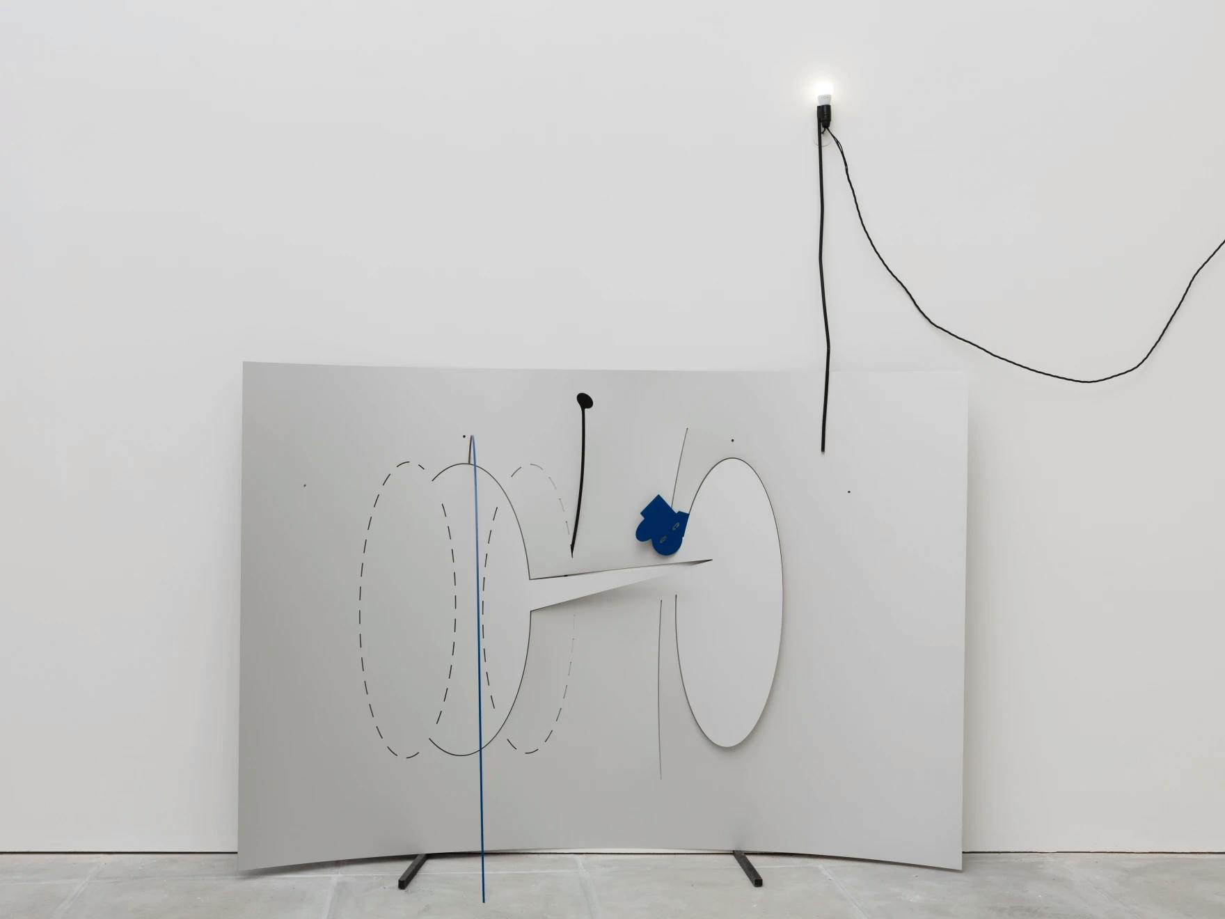 A piece of metal is perforated to suggest speech bubbles and it leans against a white wall. A light bulb is fixed to the wall illuminating the installation.