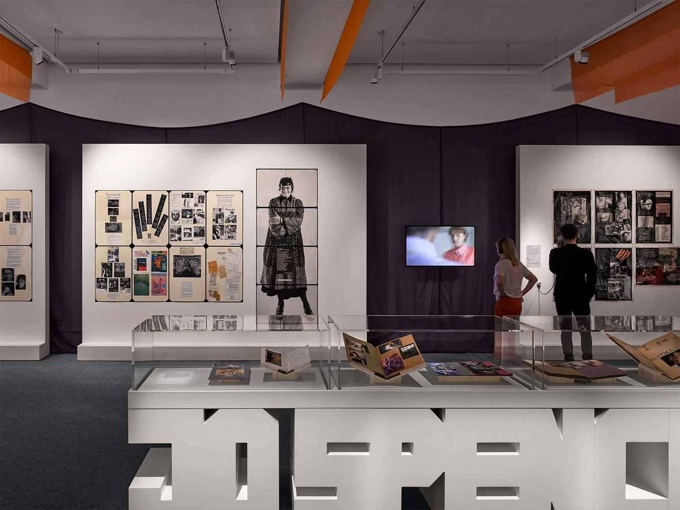 The foreground contains a vitrine sculpted in Jo Spence's name. The background contains photographs of Jo Spence on large laminated collages.