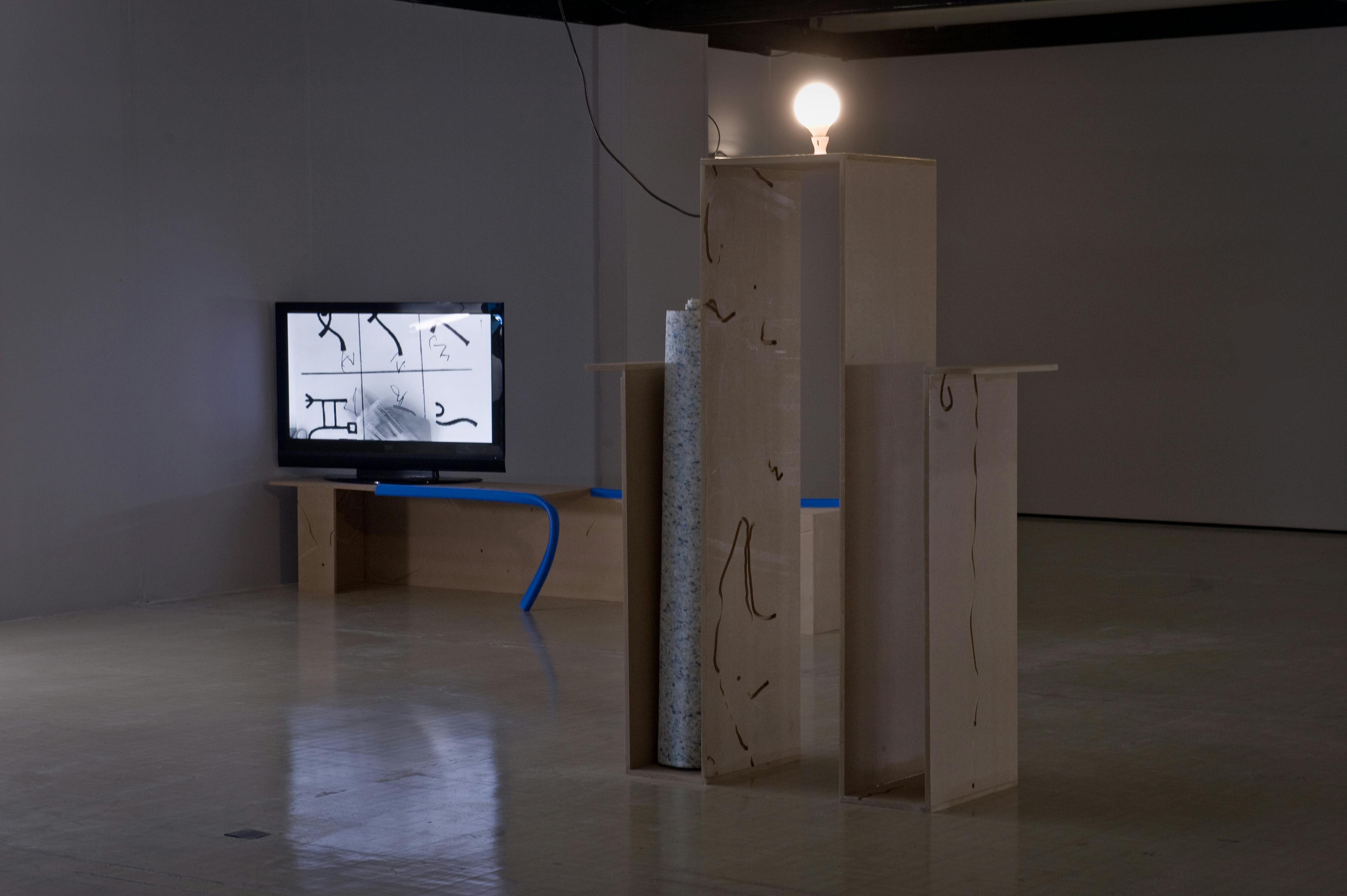 An MDF construction the size of a human being is illuminated by a single lightbulb.