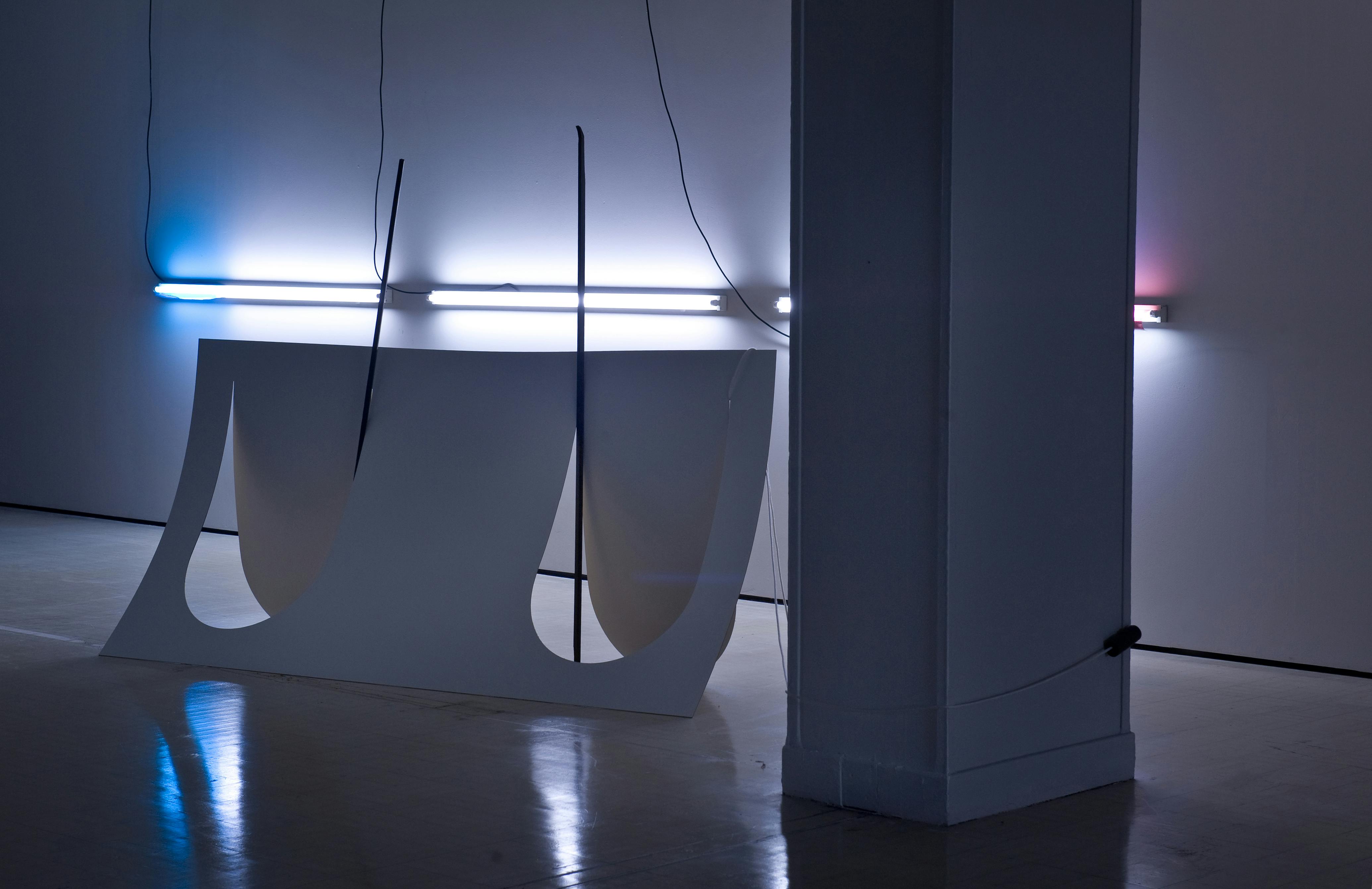Flat, thin laminated wood is cut to create a 3D form. The darkened installation is lit by strip lighting installed horizontally on the wall in the background.
